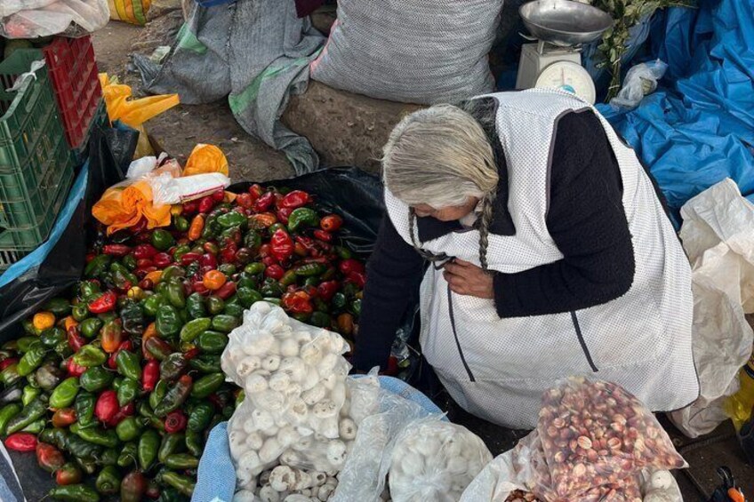 A market scene with a vendor selecting vegetables from a pile. 3