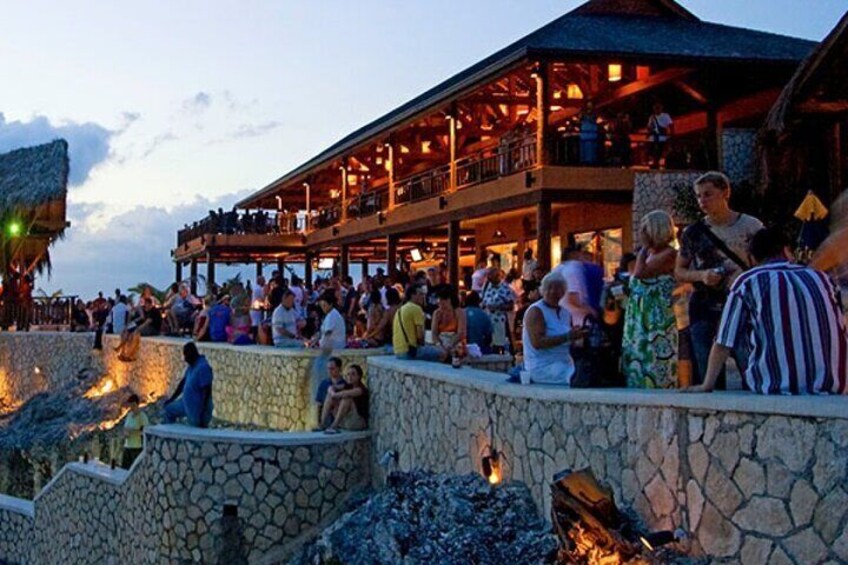 A crowded outdoor area with stone walls and a wooden structure with multiple levels. 1