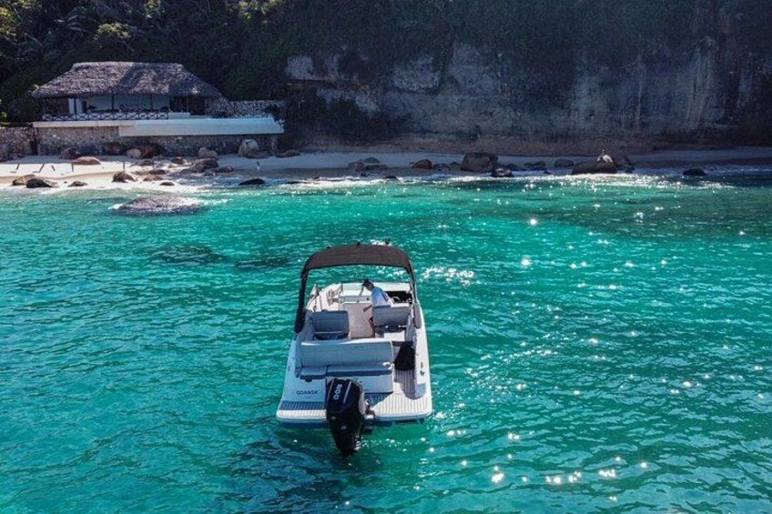 A boat on turquoise water with a rocky shoreline and a building in the background. 3