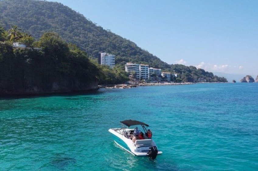 A boat on turquoise water with a mountainous coastline and buildings in the background. 2