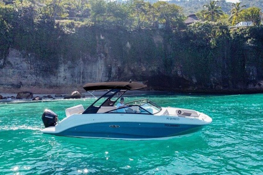 A boat on turquoise water with a rocky cliff in the background. 1
