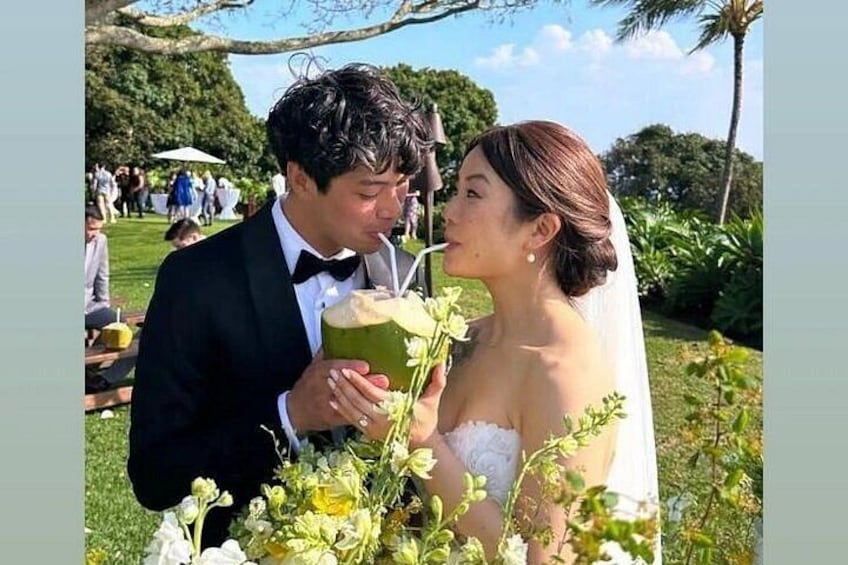 A couple in a garden, a man in a suit and a woman in a wedding dress, holding a drink. 5