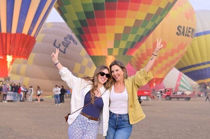 Two people posing in front of colorful hot air balloons with the words 'Easy' and 'SALEN' visible. 2