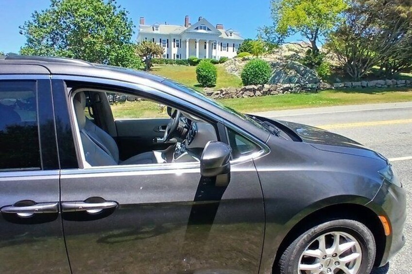A silver car parked on a street with a large house in the background. 2