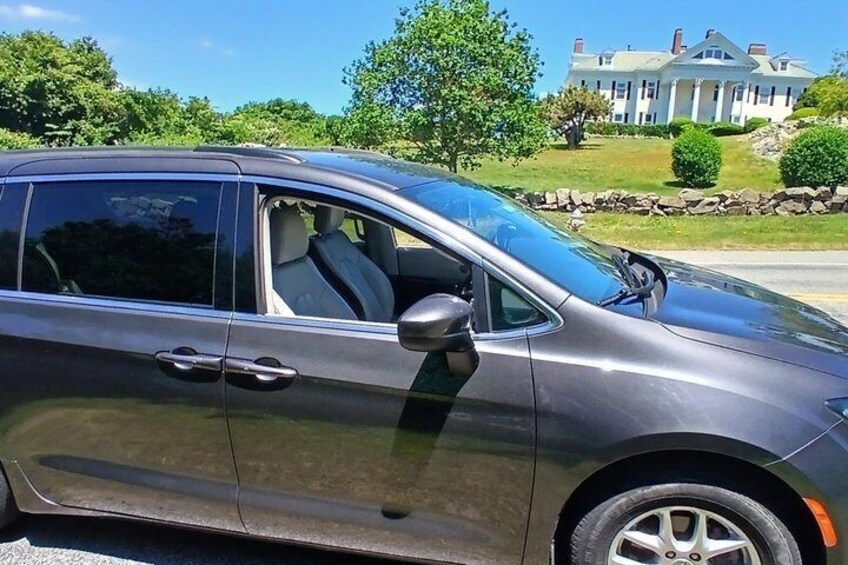 A dark-colored SUV parked on a street with a large, historic house in the background. 3