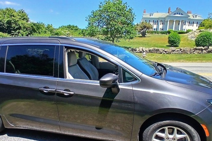 A dark-colored SUV parked on a street with a large house in the background. 2