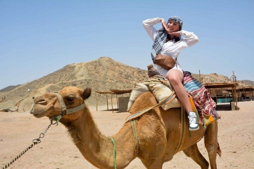 A person riding a camel in a desert with mountains in the background. 3