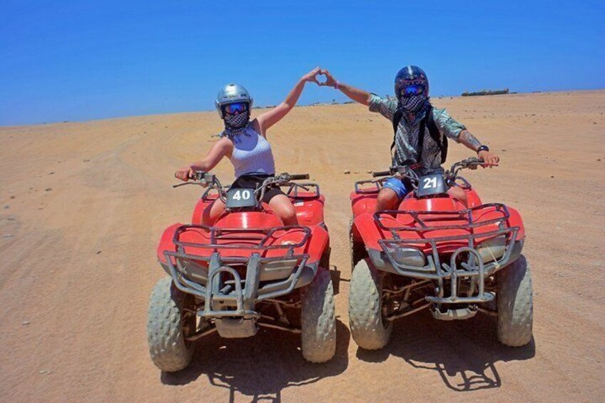 Two people on red ATVs in a desert with a clear sky. 1