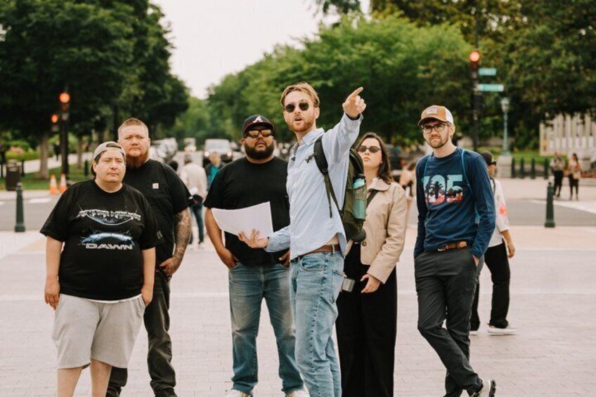 A group of people standing on a city sidewalk with trees and buildings in the background. 4
