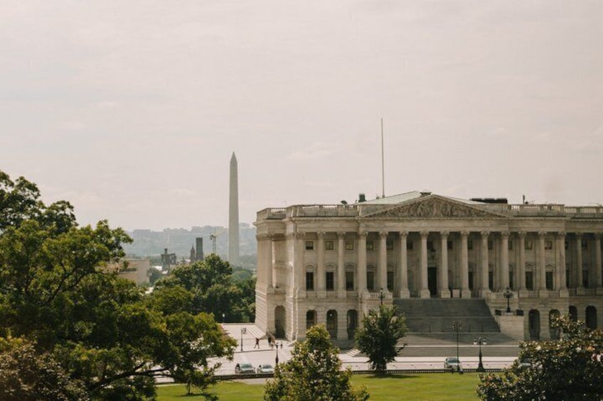A neoclassical building with columns, a large obelisk in the background, and surrounding greenery. 3