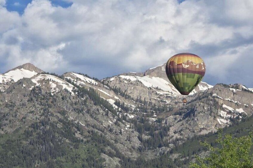 A hot air balloon over a mountainous landscape with snow-capped peaks and forested areas. 1