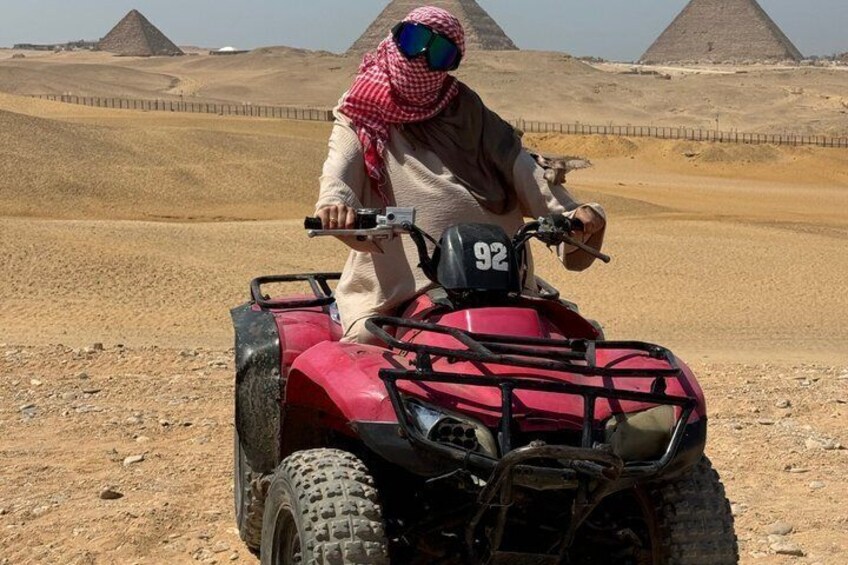 A person riding a red ATV with the number 92 in a desert landscape with pyramids in the background. 2