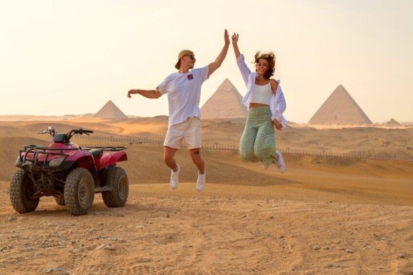 Two people jumping in front of the pyramids with an ATV in the foreground. 5