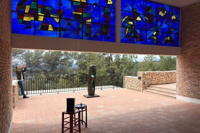A covered patio with a stained glass window, a sculpture, and a person taking a photo. 4