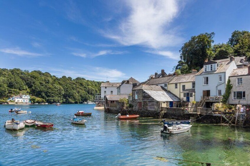 A coastal village with boats on calm water, houses by the shore, and a forested hill in the background. 3