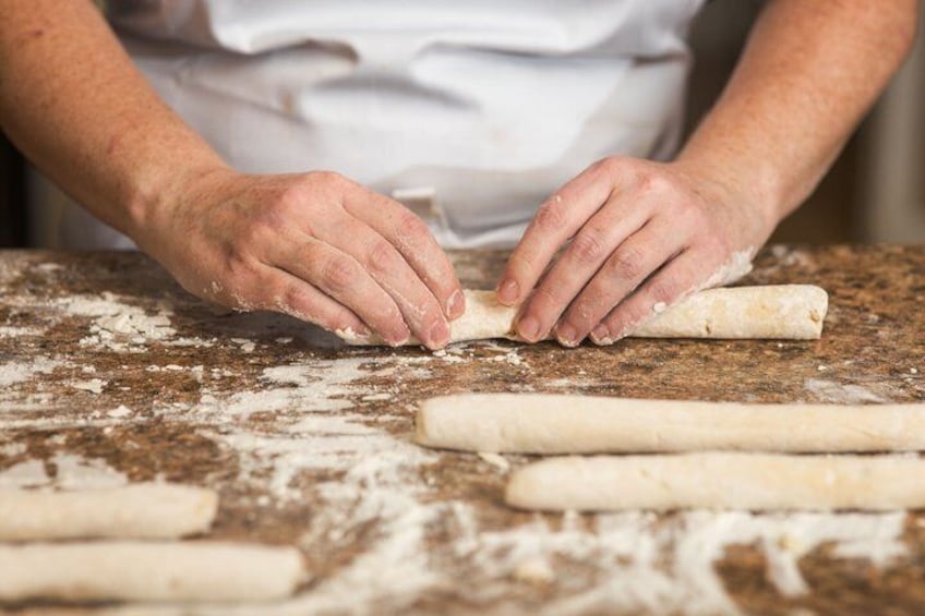 A person rolling dough on a floured surface with additional dough pieces nearby. 3