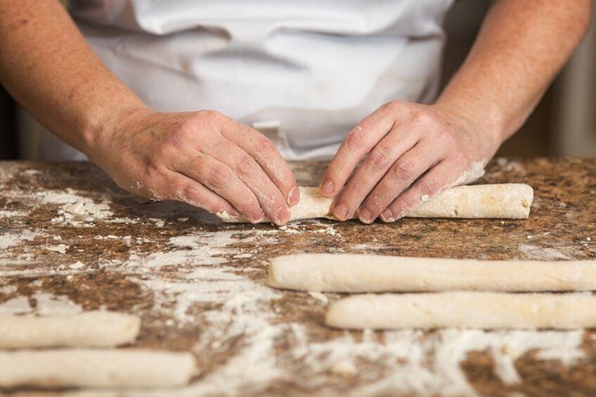 Hands rolling dough on a floured surface with additional dough sticks nearby. 2