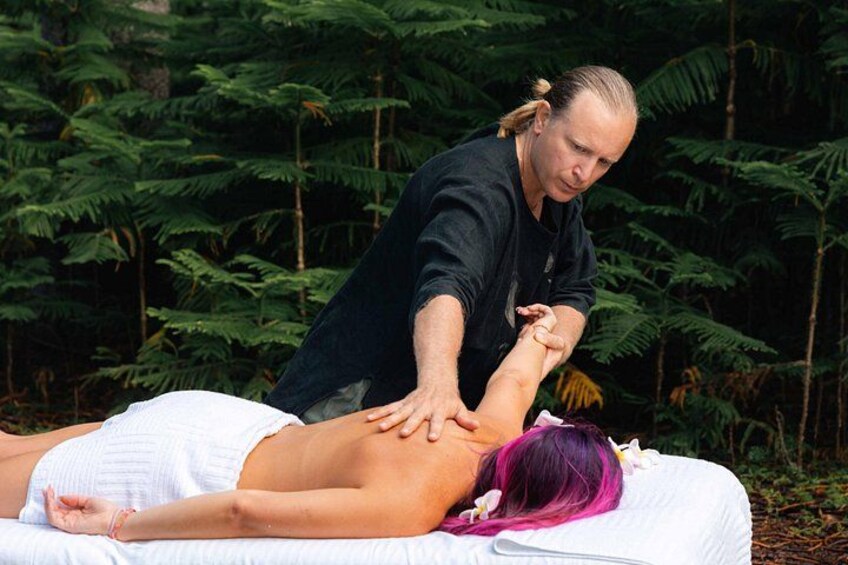 A person receiving a massage outdoors with dense green foliage in the background. 1