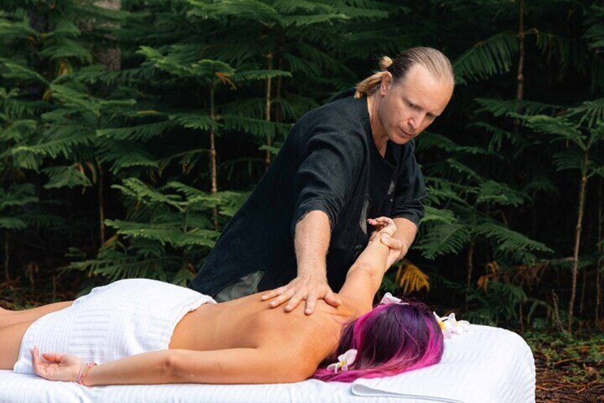 A person receiving a massage outdoors with dense green foliage in the background. 1
