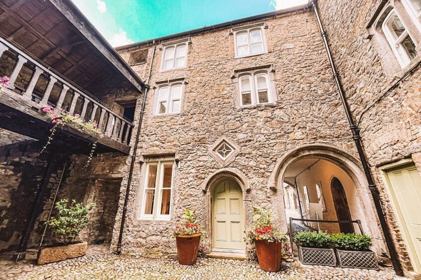A stone building with a wooden balcony, a central door, and potted plants. 3