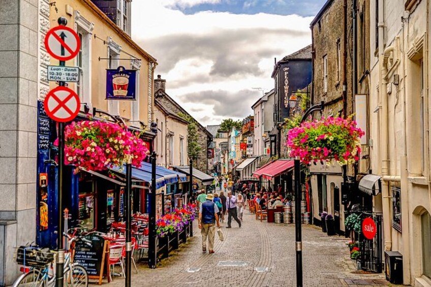 A cobblestone street lined with shops, hanging flower baskets, and a 'No Parking' sign. 1