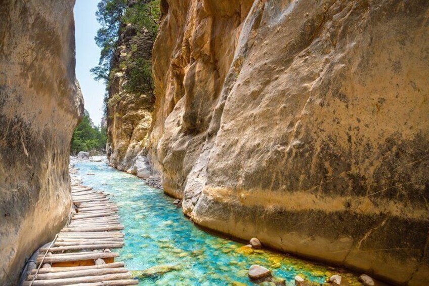 A narrow canyon with a wooden walkway and a clear blue river. 1