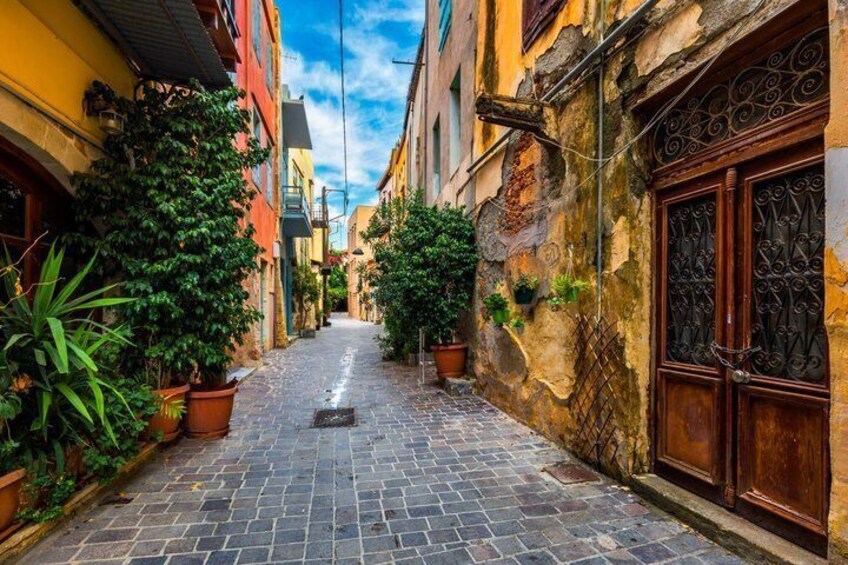 A narrow cobblestone alley flanked by buildings with potted plants and a wrought iron gate. 5