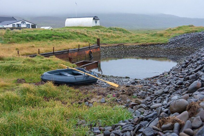 A riverbank with a raft, a paddle, and a small house in the background. 2