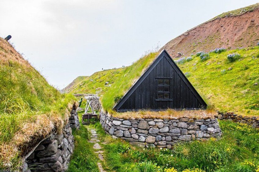 A black wooden house with a stone wall and a grassy hill in the background. 5