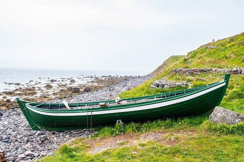 A green boat on a rocky shore with grass and a hill in the background. 4