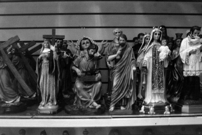 A group of statues in various poses, some holding crosses, set against a plain background. 3