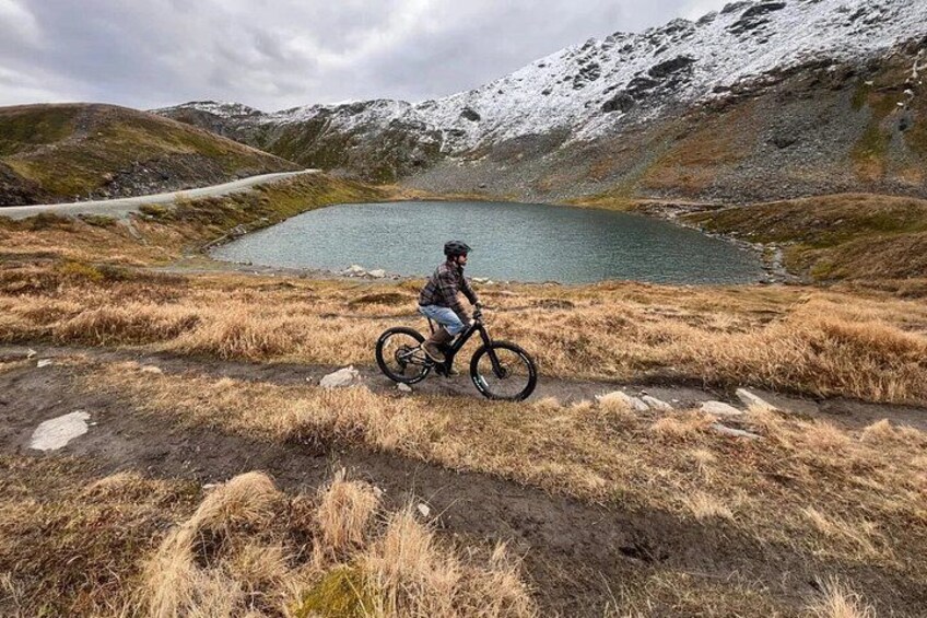 A person on a mountain bike near a lake with snow-capped mountains in the background. 4