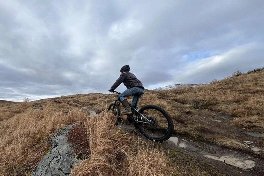 A person riding a mountain bike on a dirt trail with grassy terrain and a cloudy sky. 5