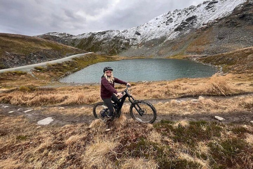 A person on a mountain bike near a lake with snow-capped mountains in the background. 4