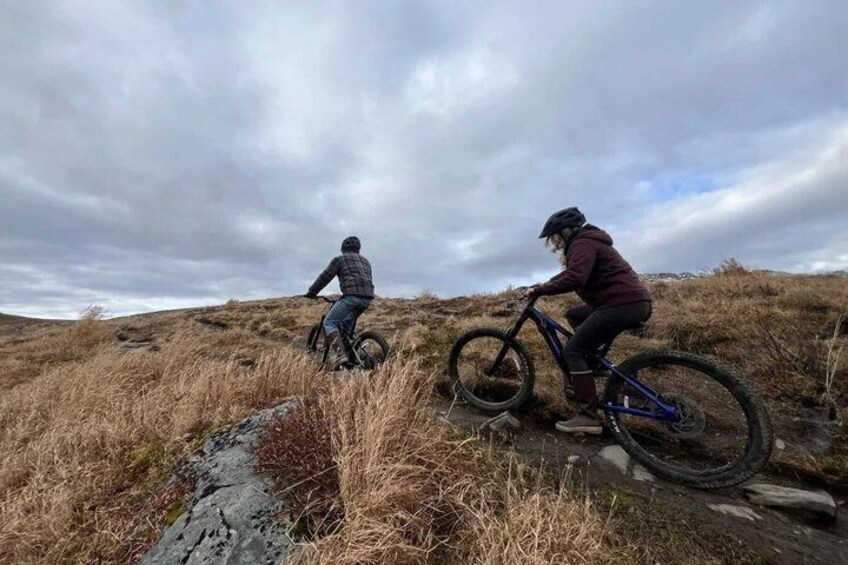 Two cyclists on a grassy hill with a cloudy sky. 5