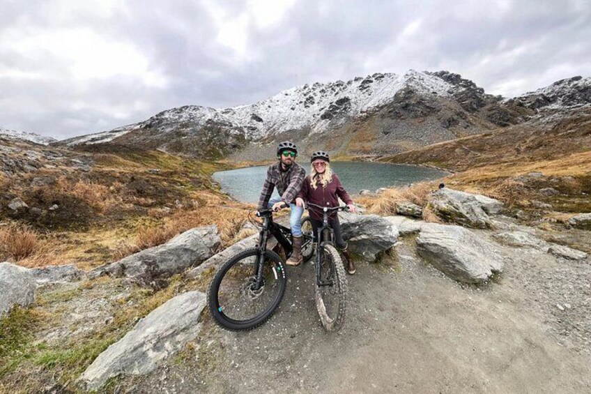 Two people on mountain bikes in a rocky, mountainous landscape with a lake in the background. 2