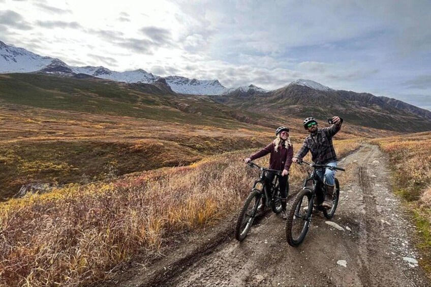 Two people on mountain bikes on a dirt trail with mountains in the background. 4