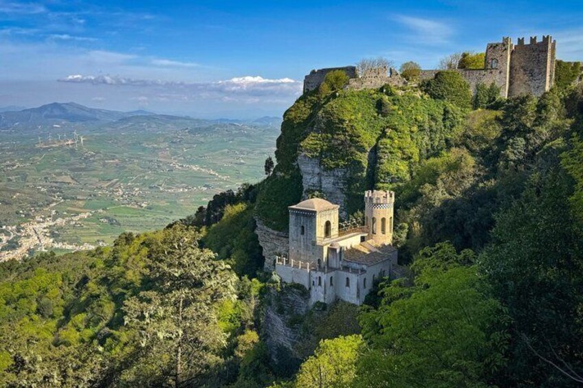 A castle on a hill with a church below, surrounded by greenery and a valley. 1