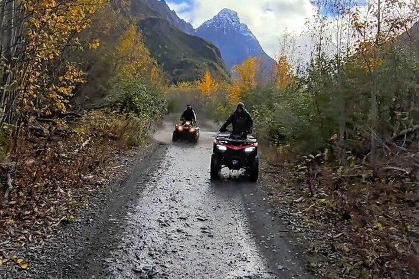 Two ATVs on a gravel road surrounded by autumn foliage and mountains. 4