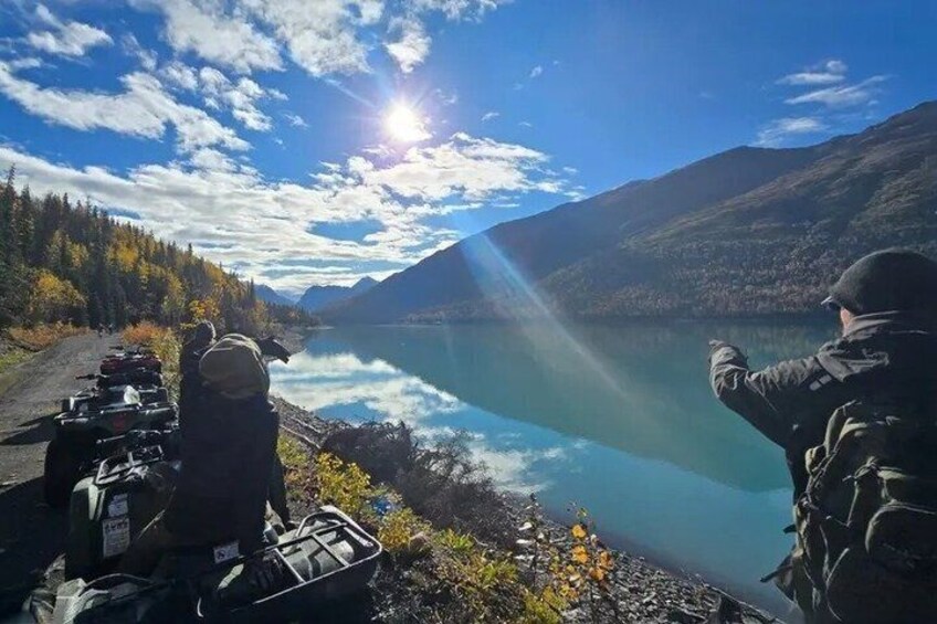 A lake with mountains in the background, a clear sky, and a person pointing towards the water. 2