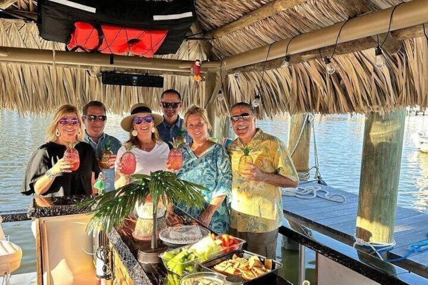 A group of people on a boat with a thatched roof, holding drinks and a plant. 4