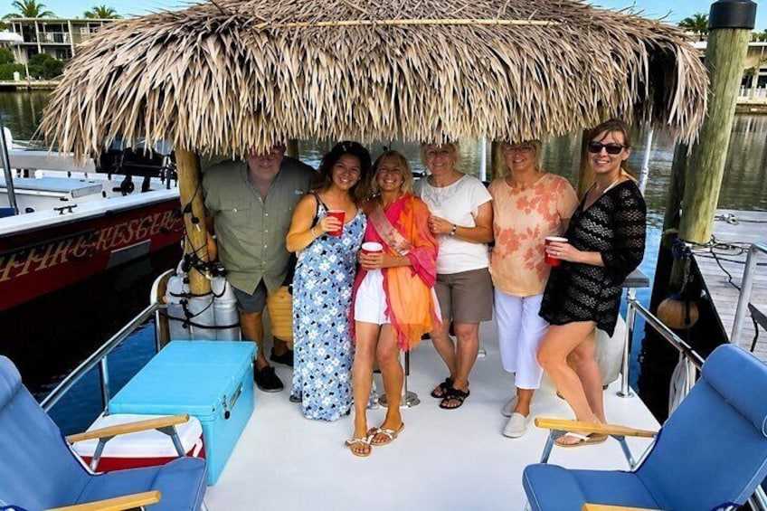 A group of people on a boat with a thatched roof, surrounded by water and docked near a building. 2