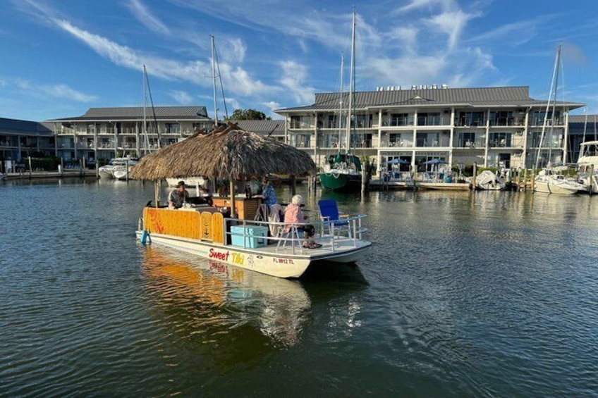 A boat with a thatched roof and 'Sweet Tiki' branding, docked at a marina with buildings in the background. 5