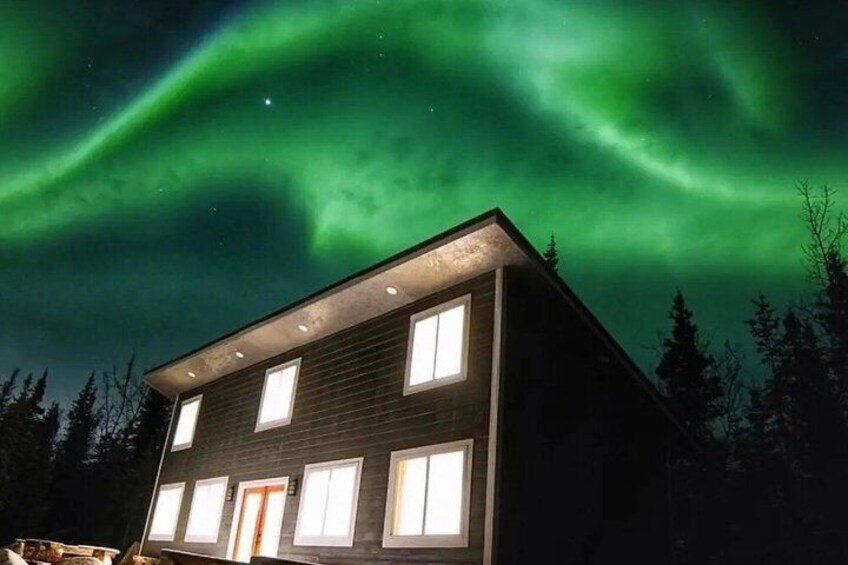 A house with multiple windows and a door, surrounded by trees under a night sky with green aurora. 3
