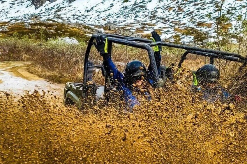 A vehicle navigating through a muddy terrain with two people inside. 2