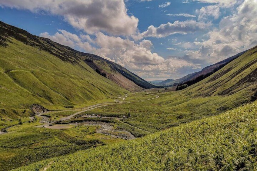 A valley with a winding road, green hills, and a clear sky. 1