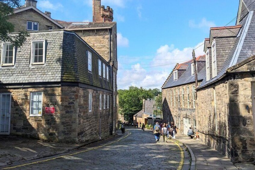 A cobblestone street lined with historic stone buildings, a clear sky, and pedestrians walking. 2