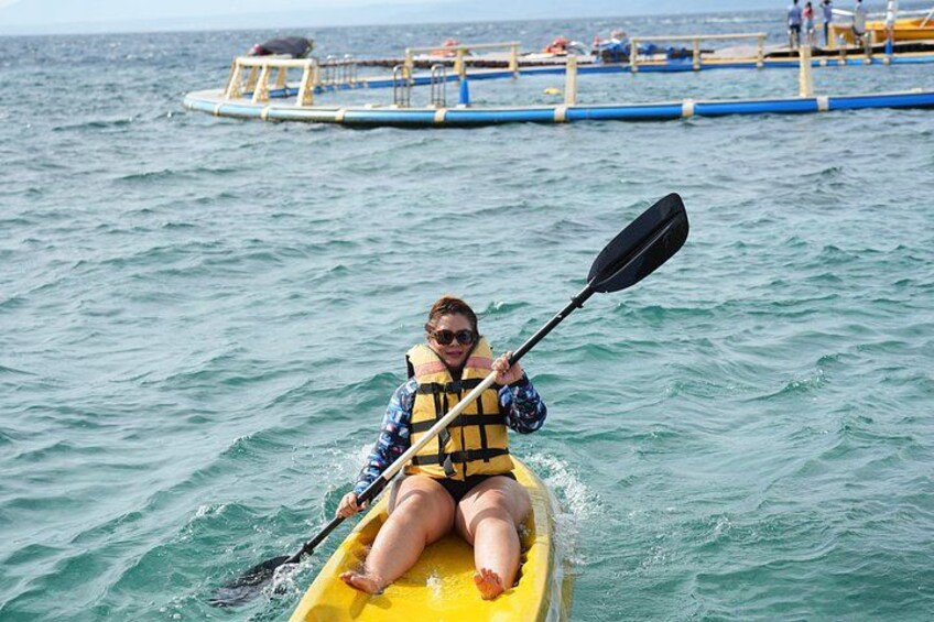 A person kayaking on a yellow kayak in the ocean, with a dock and people in the background. 4