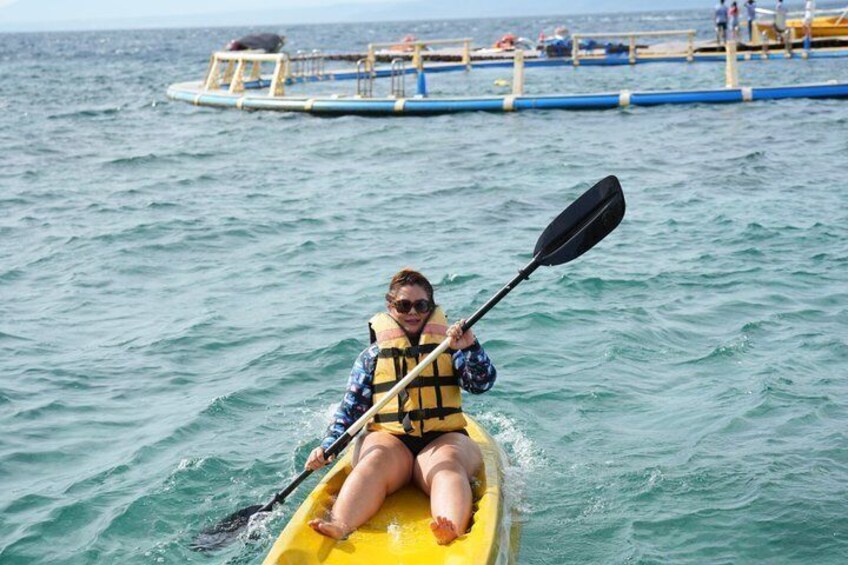 A person kayaking on a yellow raft in the ocean with a dock and people in the background. 4