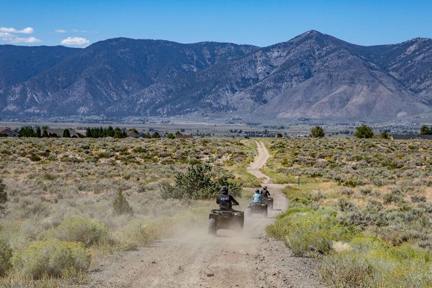 A dirt road with ATVs, surrounded by sparse vegetation and mountains in the background. 2